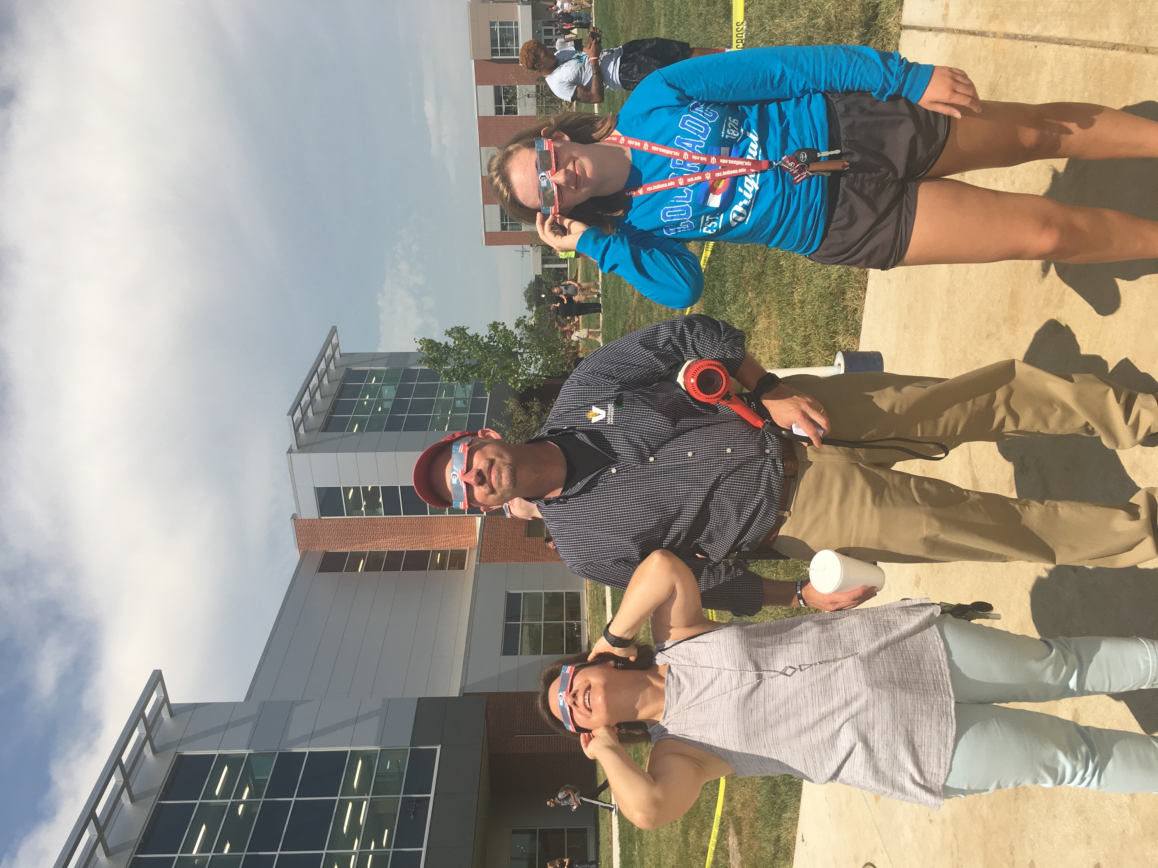 VU Dean Curt Coffman and 2 females, all wearing solar eclipse glasses, look up at the sky while standing near Updike Hall during the 2017 total solar eclipse. 